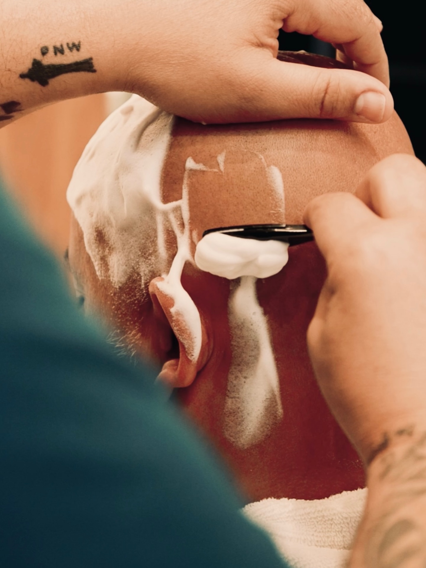 A barber applying lather along a client's ear and neck before a straight razor shave